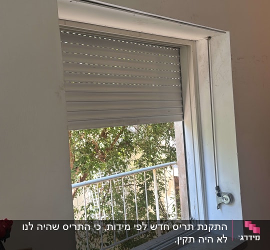 חלון עם תריס גלילה פתוח חלקית ונוף עצים בחוץ